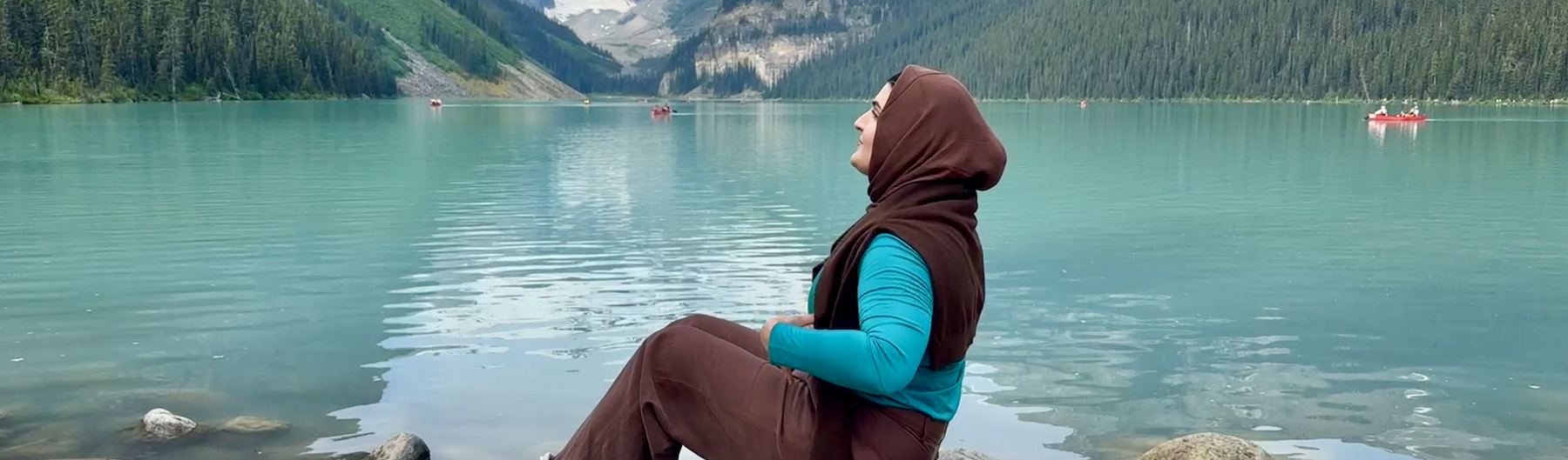 Nazia sitting at the edge of a still mountain lake